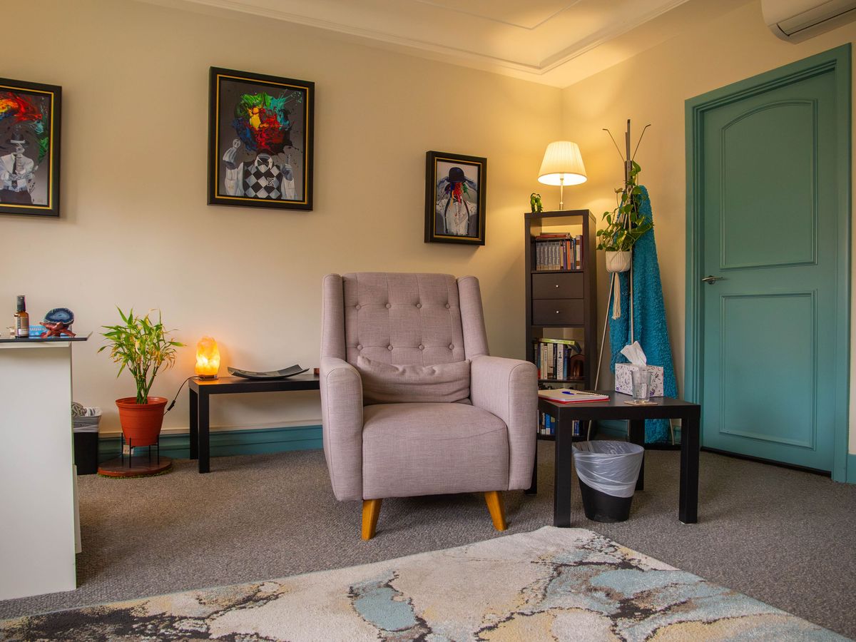 The consulting room: an armchair beneath framed artwork, beside a teal door