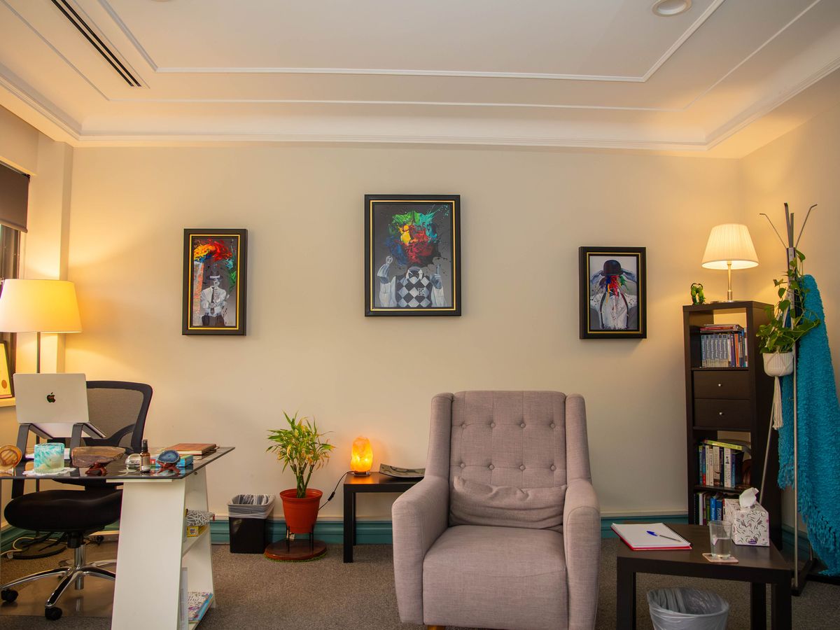 The consulting room, with an armchair, a desk and a bookshelf beneath framed artwork